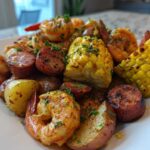 A close-up of a plated, seasoned shrimp boil featuring shrimp, corn on the cob, smoked sausage, and red potatoes.