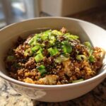 A close-up of a hearty serving of egg roll in a bowl, garnished generously with sliced green onions and sesame seeds.