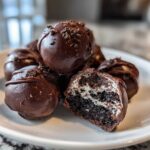 A pile of decadent chocolate-covered Oreo balls, one cut in half showing the dark cookie and cream filling.