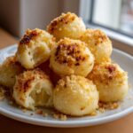 A pile of fluffy potato dumplings coated in toasted breadcrumbs served on a white plate.