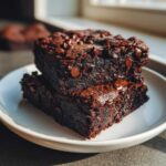 Two moist, fudgy black bean brownies stacked on a white plate, topped with melted chocolate chips.