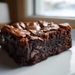 A close-up of a dense, fudgy slice of Oreo brownies with a shiny, crackly top.