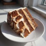 A tall slice of multi-layered gingerbread latte cake with white and brown marbled frosting.