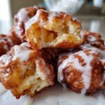 Close-up of several golden brown, glazed apple fritter pieces piled on a plate, showing the soft, apple-filled interior.