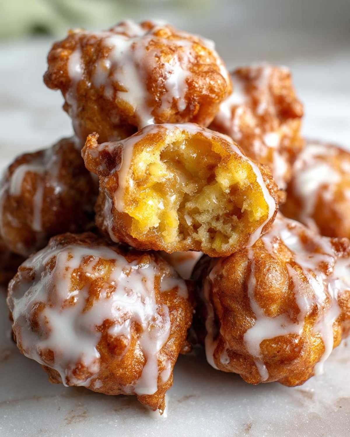 Close-up of a stack of golden brown, glazed apple fritter pieces, one broken open to show the soft, apple-filled interior.