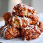 A tempting stack of golden brown apple fritter pieces drizzled heavily with white vanilla glaze.