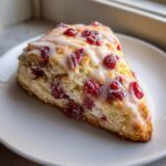 A single wedge of fluffy cranberry scones topped with a sweet white glaze, sitting on a white plate.