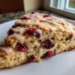 A close-up, triangular slice of a freshly baked cranberry scones topped with white vanilla glaze.