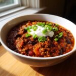 Close-up of a hearty bowl of pumpkin chili topped with sour cream and green onions.