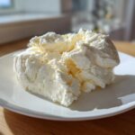 A generous scoop of creamy, pale yellow cottage cheese ice cream served on a white plate.