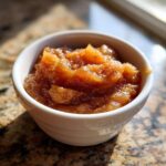 A close-up, appetizing shot of chunky homemade applesauce seasoned with cinnamon in a small white bowl.