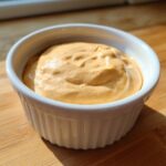 Close-up of creamy, orange-tinted big mac sauce served in a small white fluted bowl on a wooden surface.