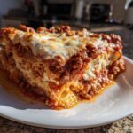 A thick, layered slice of homemade lasagna with rich meat sauce and melted mozzarella cheese on a white plate.