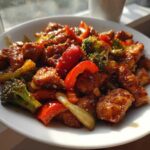 Close-up of glistening honey garlic chicken stir fry with broccoli and red bell peppers served in a white bowl.