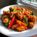 Close-up of glistening honey garlic chicken stir fry mixed with bright red peppers and green broccoli florets.