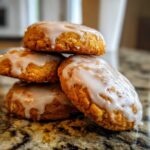 A stack of four soft, spiced persimmon cookies topped with a thick white glaze, resting on a granite countertop.