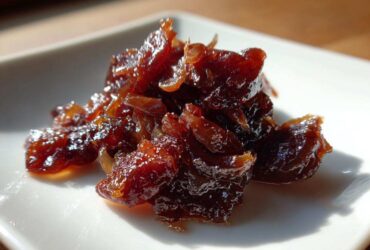 Close-up of a small pile of deep brown, glossy caramelized onions on a white square plate.