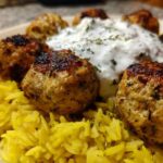 Close-up of perfectly browned greek chicken meatballs served over yellow rice with a dollop of tzatziki sauce.