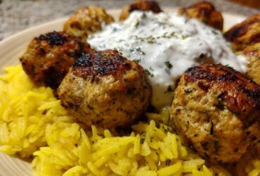 Close-up of perfectly browned greek chicken meatballs served over yellow rice with a dollop of tzatziki sauce.