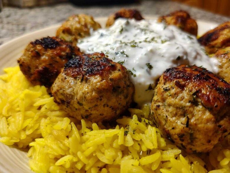 Close-up of perfectly browned greek chicken meatballs served over yellow rice with a dollop of tzatziki sauce.