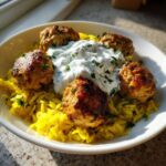 Five golden brown greek chicken meatballs served over bright yellow rice, topped with a dollop of creamy tzatziki sauce.