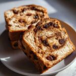 Close-up of two thick slices of homemade raisin bread with visible cinnamon swirl and plump raisins.