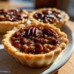 Close-up of a freshly baked mini pecan pie with a glossy filling and whole pecans on top.