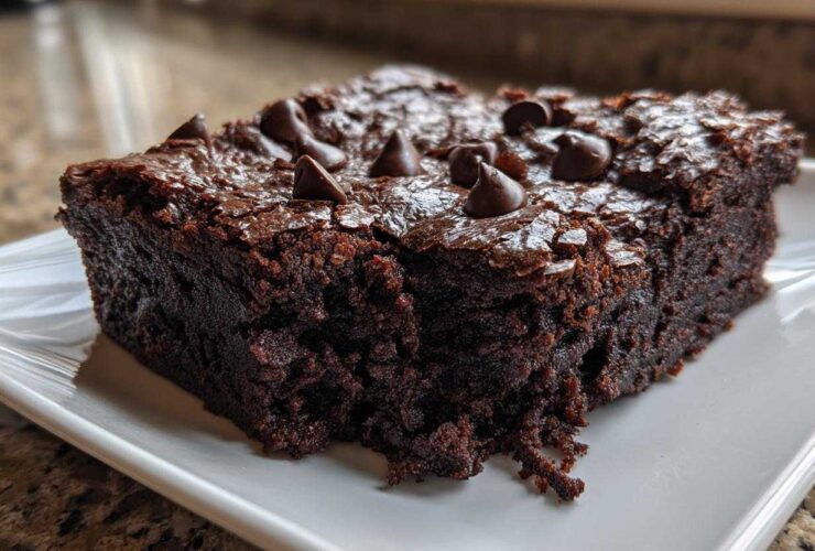A close-up of a rich, fudgy slice of black bean brownies topped with melted chocolate chips on a white plate.