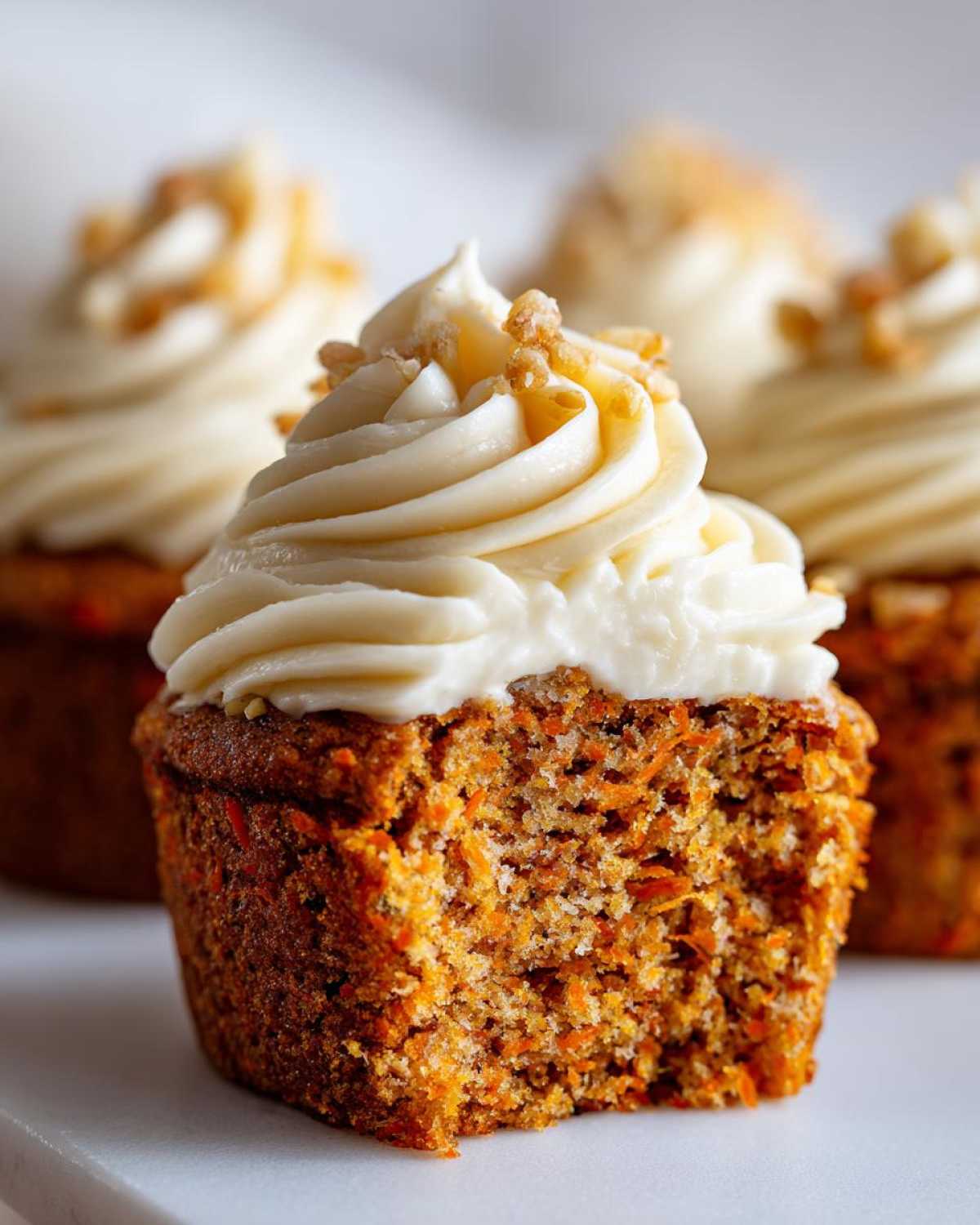 Close-up of a moist carrot cake muffins cut in half showing texture, topped with cream cheese frosting and nuts.