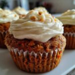 Close-up of moist carrot cake muffins topped with thick cream cheese frosting and chopped nuts.