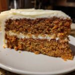 Close-up of a moist slice of carrot cake recipe with visible shredded carrots and thick cream cheese frosting.