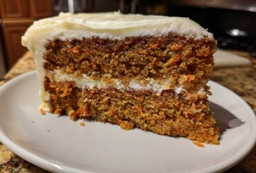 Close-up of a moist slice of carrot cake recipe with visible shredded carrots and thick cream cheese frosting.