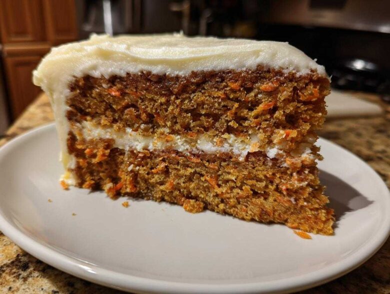 Close-up of a moist slice of carrot cake recipe with visible shredded carrots and thick cream cheese frosting.