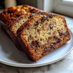 Close-up of three slices of moist banana bread recipe studded with melted chocolate chips, served on a white plate.