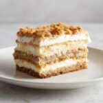 Close-up of a layered slice of moist coconut cake featuring cream filling and a crunchy crumble topping.
