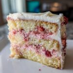 Close-up of a moist slice of three-layer strawberry cake with white frosting and visible fresh strawberry filling.
