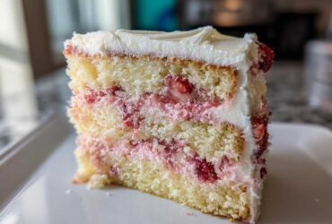 Close-up of a moist slice of three-layer strawberry cake with white frosting and visible fresh strawberry filling.