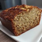 A close-up view of a freshly baked slice of moist hawaiian banana bread with a dark, caramelized crust.