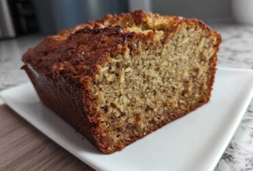 A close-up view of a freshly baked slice of moist hawaiian banana bread with a dark, caramelized crust.