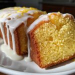 Close-up of a moist lemon pound cake, sliced to show the crumb, covered in white glaze and lemon zest.