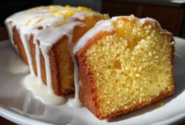 Close-up of a moist lemon pound cake, sliced to show the crumb, covered in white glaze and lemon zest.