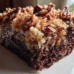 Close-up of a rich slice of german chocolate poke cake topped with gooey coconut and pecan frosting.