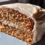 Close-up of a thick slice of moist spice cake with creamy frosting speckled with spices.