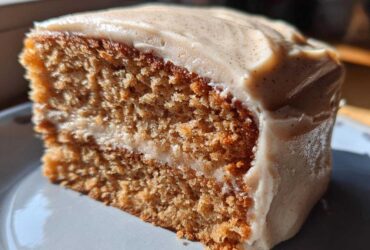 Close-up of a thick slice of moist spice cake with creamy frosting speckled with spices.