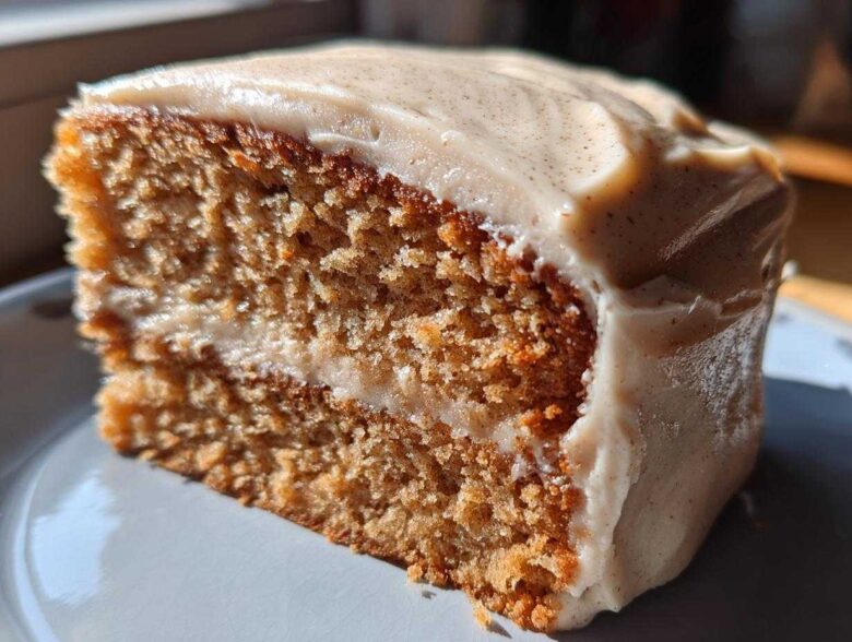 Close-up of a thick slice of moist spice cake with creamy frosting speckled with spices.