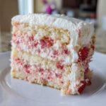 Close-up of a moist slice of strawberry cake with layers of white cake, strawberry filling, and whipped cream frosting.
