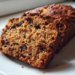 Close-up of two slices of moist vegan banana bread with visible chocolate chips on a white plate.