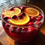 Close-up of a sparkling non-alcoholic Christmas punch garnished with bright orange slices and whole cranberries.
