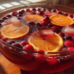 Close-up of a vibrant non-alcoholic Christmas punch in a glass bowl, garnished with orange slices, fresh cranberries, and ice cubes.