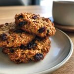 A stack of three golden brown oatmeal raisin cookies resting on a light ceramic plate.